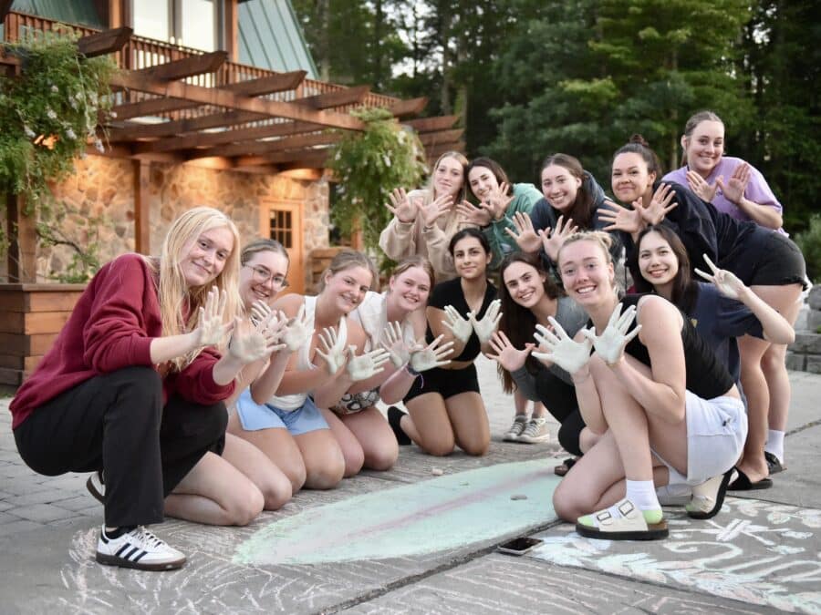 A group of girls surround a drawing made from chalk, while demonstrating the Kount on Kindness logo.