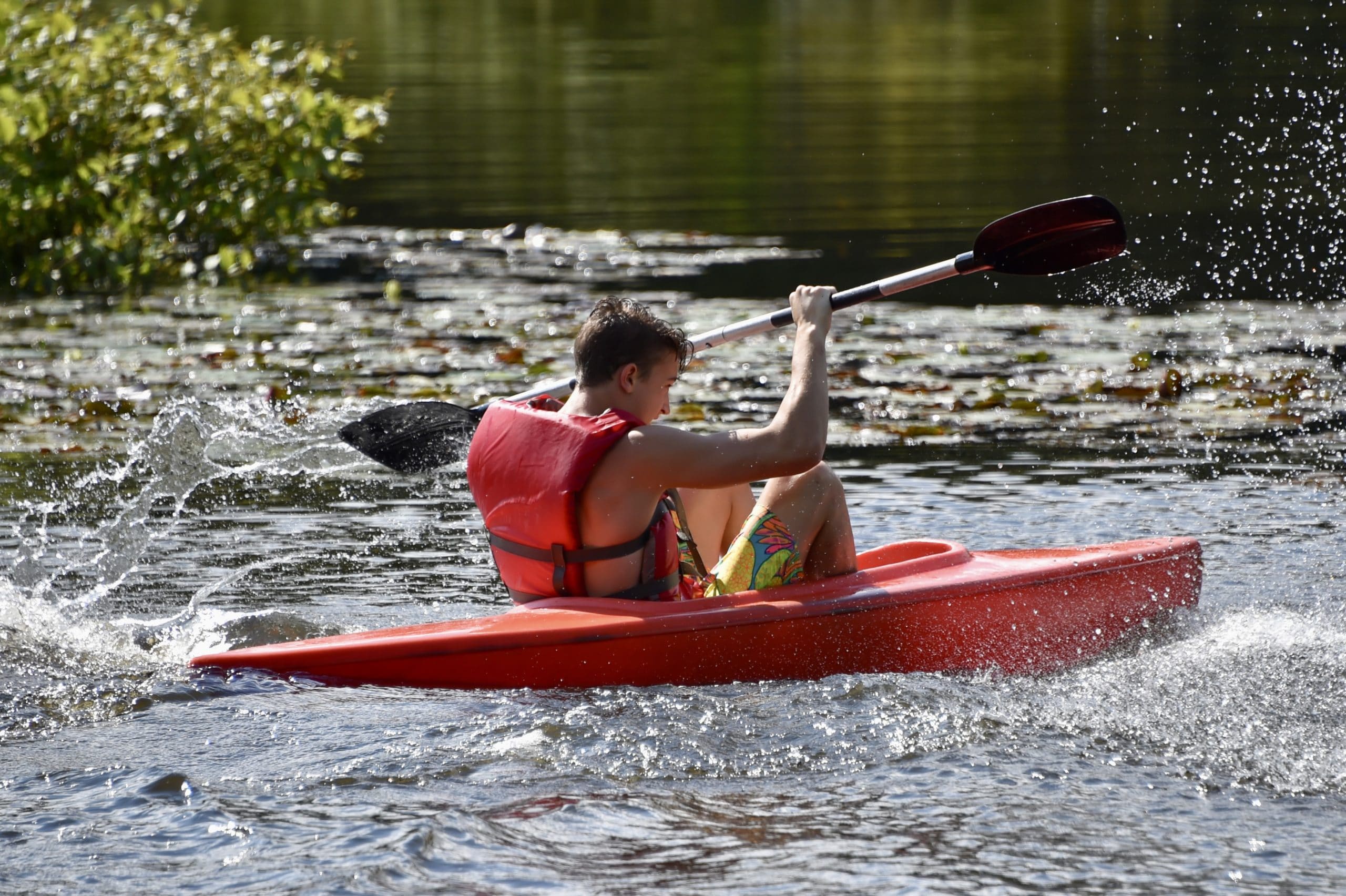 A camper kayaks on a body of water while wearing a life vest.
