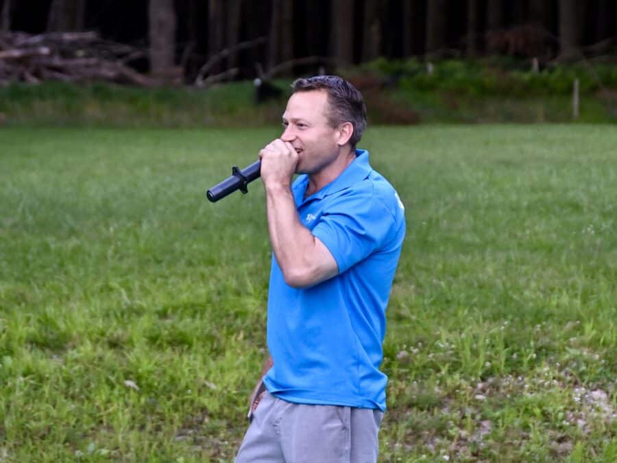 An image of Brent Klaus standing while holding a microphone up to his mouth.