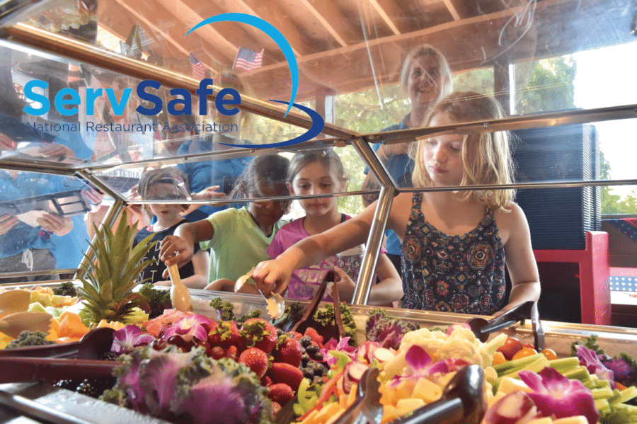 Young campers stand in a line and reach for fruit from a buffet style table.